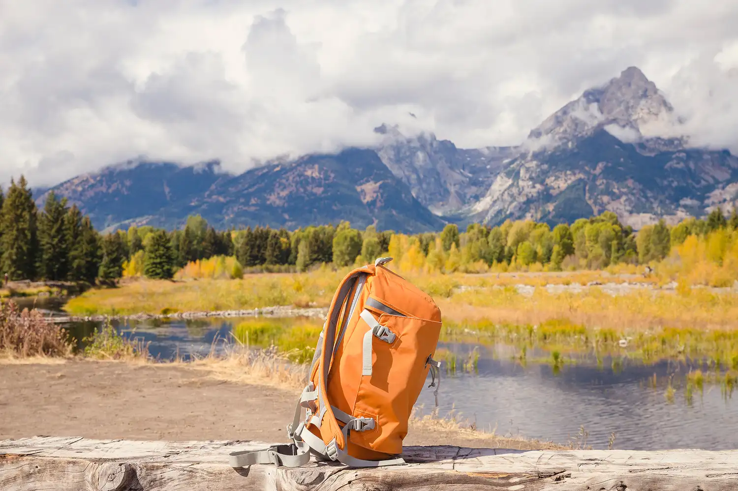 A technical hiking backpack placed on a fallen log overlooking a valley and distant mountains.