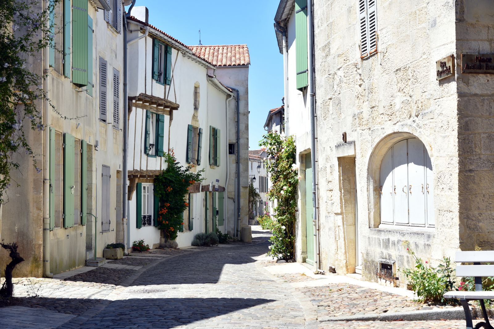 A narrow cobblestone street between white-washed buildings in a French village.