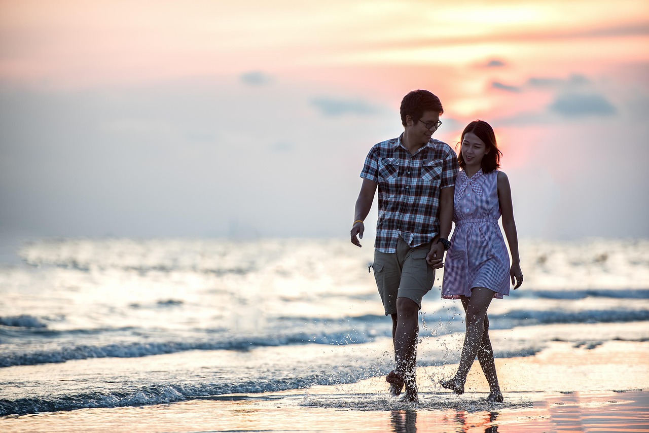 A couple in white linen clothing walking barefoot on a pristine white sand beach