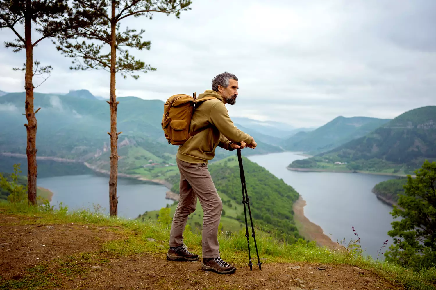 A senior man standing on a high viewpoint overlooking a peaceful lake in spring.