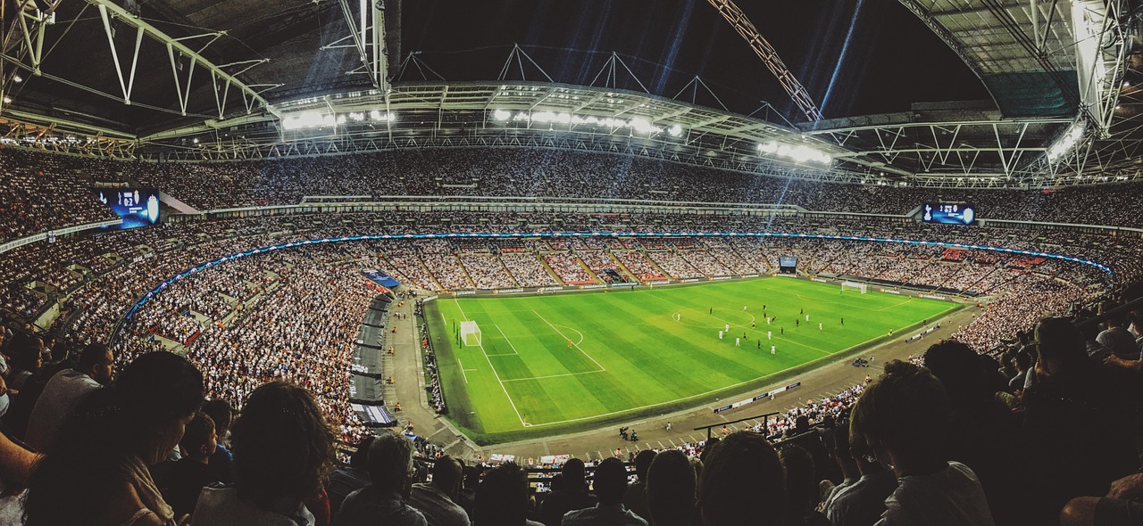 A massive modern soccer stadium filled with fans under bright lights at night.