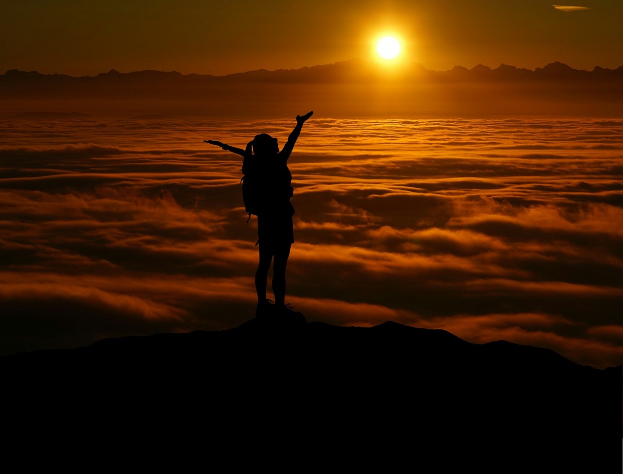 A lone woman standing on a cliff edge looking out at the horizon during dawn.