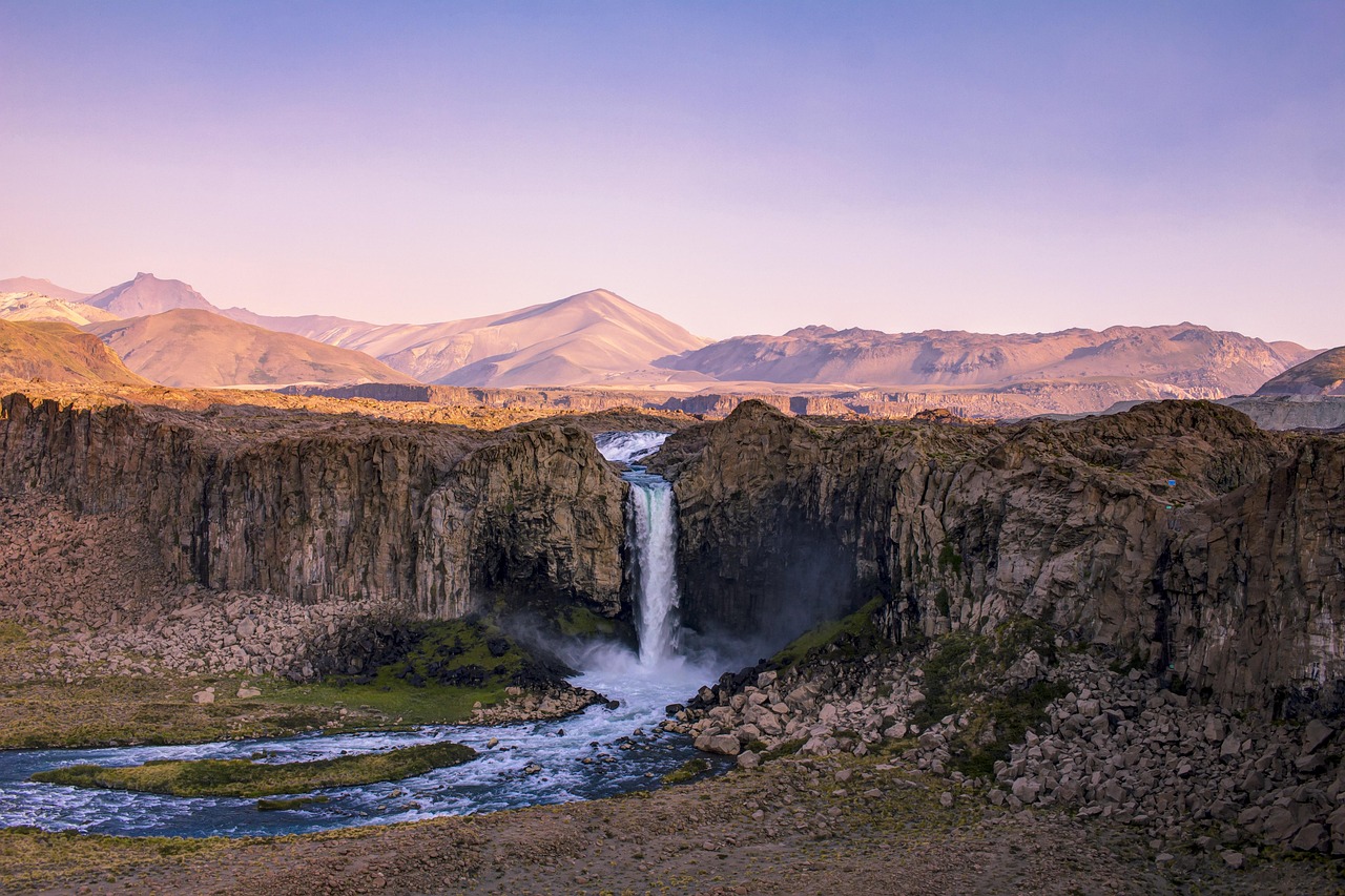 High altitude waterfall cascading down multi-tiered rock faces into a green valley