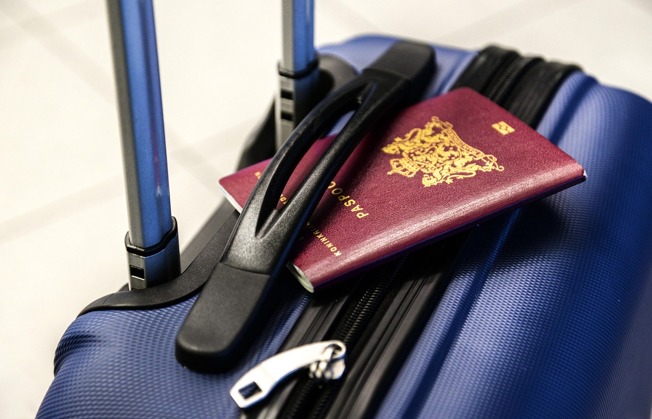 A person using a smartphone next to a passport and a suitcase to plan a trip.