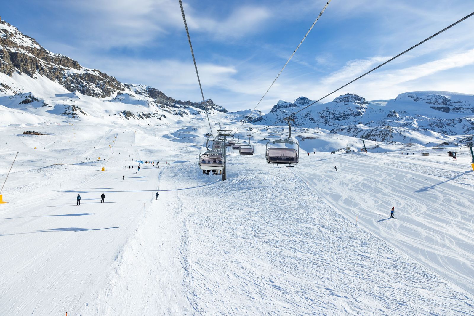A skier on a snowy slope with a ski lift and mountain range in the background.