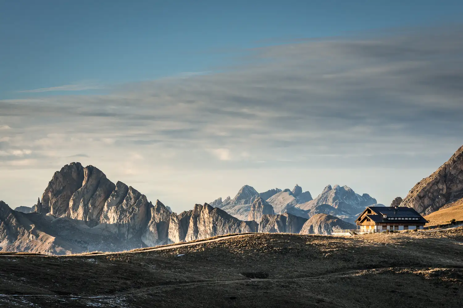 A high-altitude mountain cabin with the rugged, rocky peaks of the Dolomites in the background.