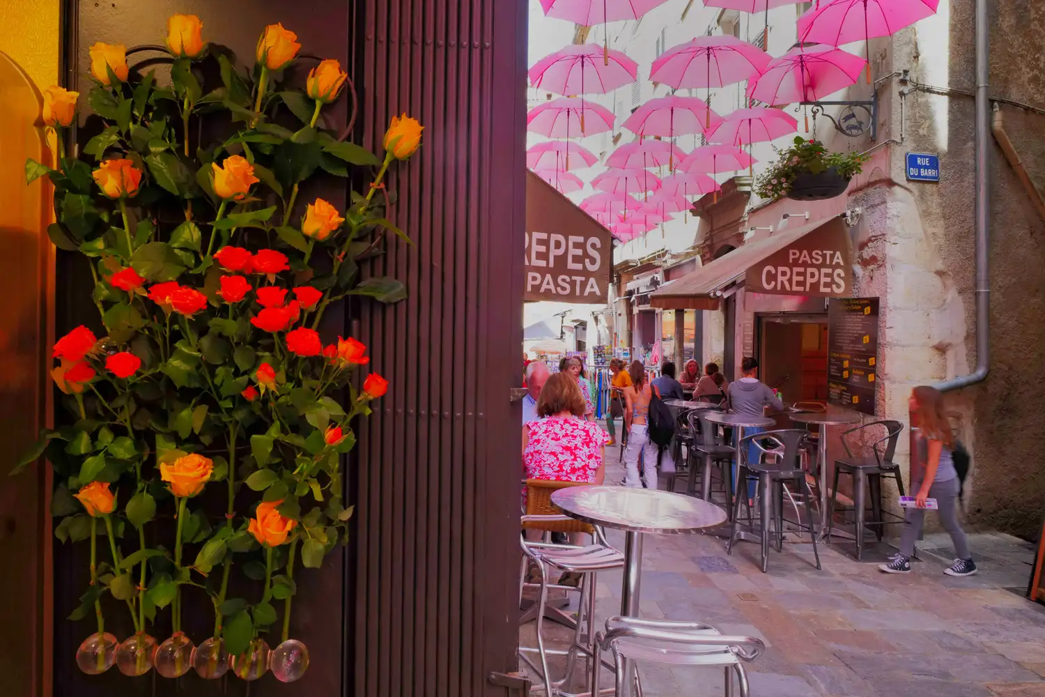 Dozens of vibrant pink umbrellas suspended above a narrow cobblestone street with outdoor cafe tables.