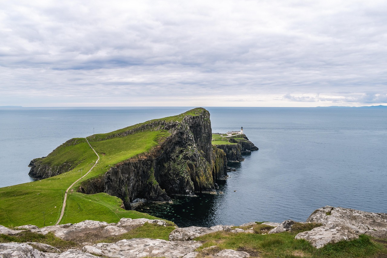 A white lighthouse on a green headland overlooking the sea