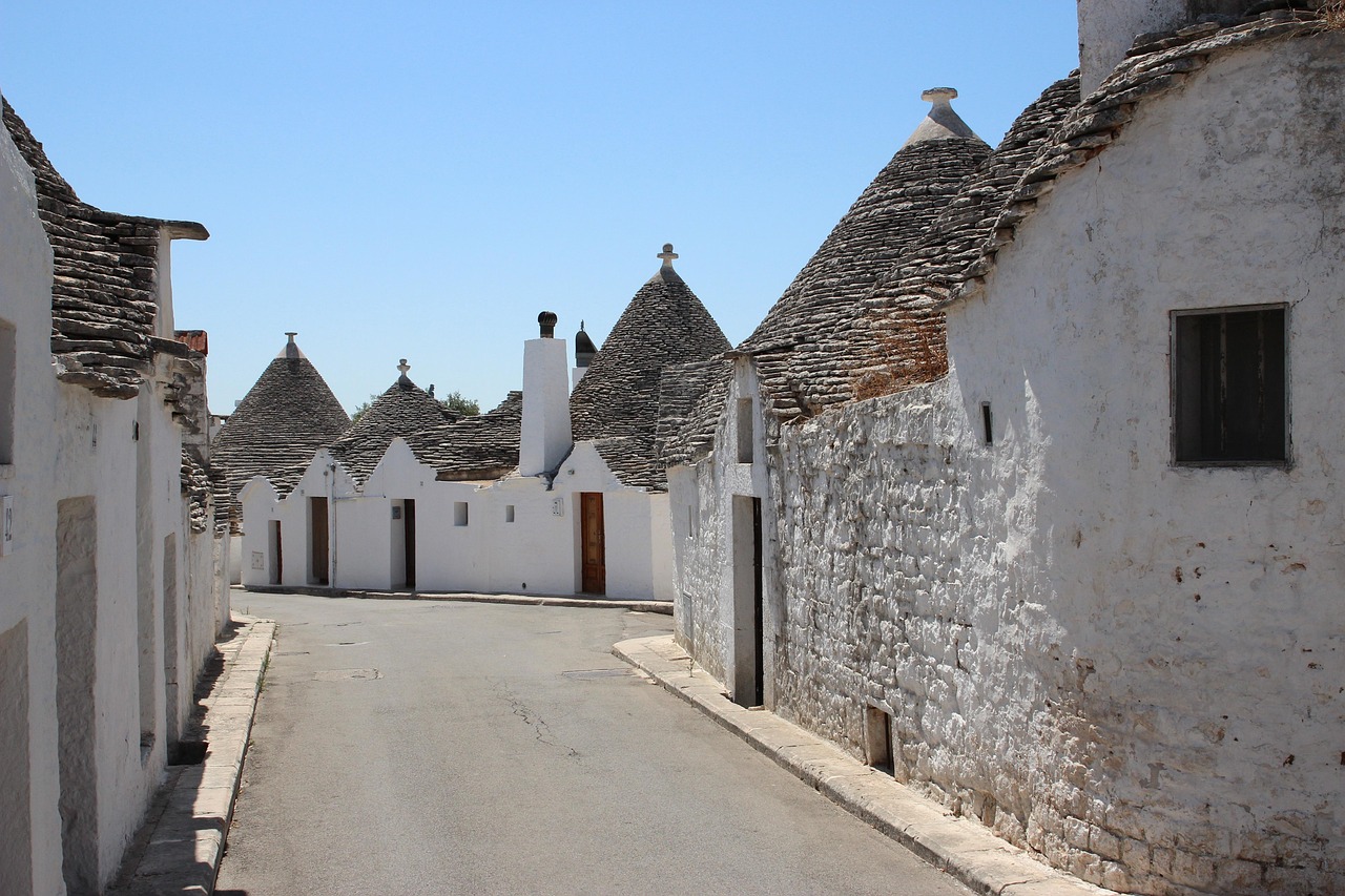 Traditional white stone trulli huts with conical roofs and mysterious symbols under a bright blue sky.