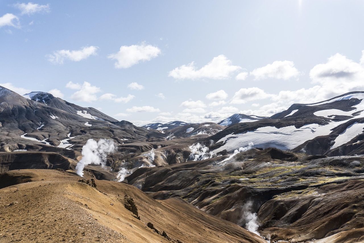 A natural steaming hot spring pool with snow-capped mountains in the background.