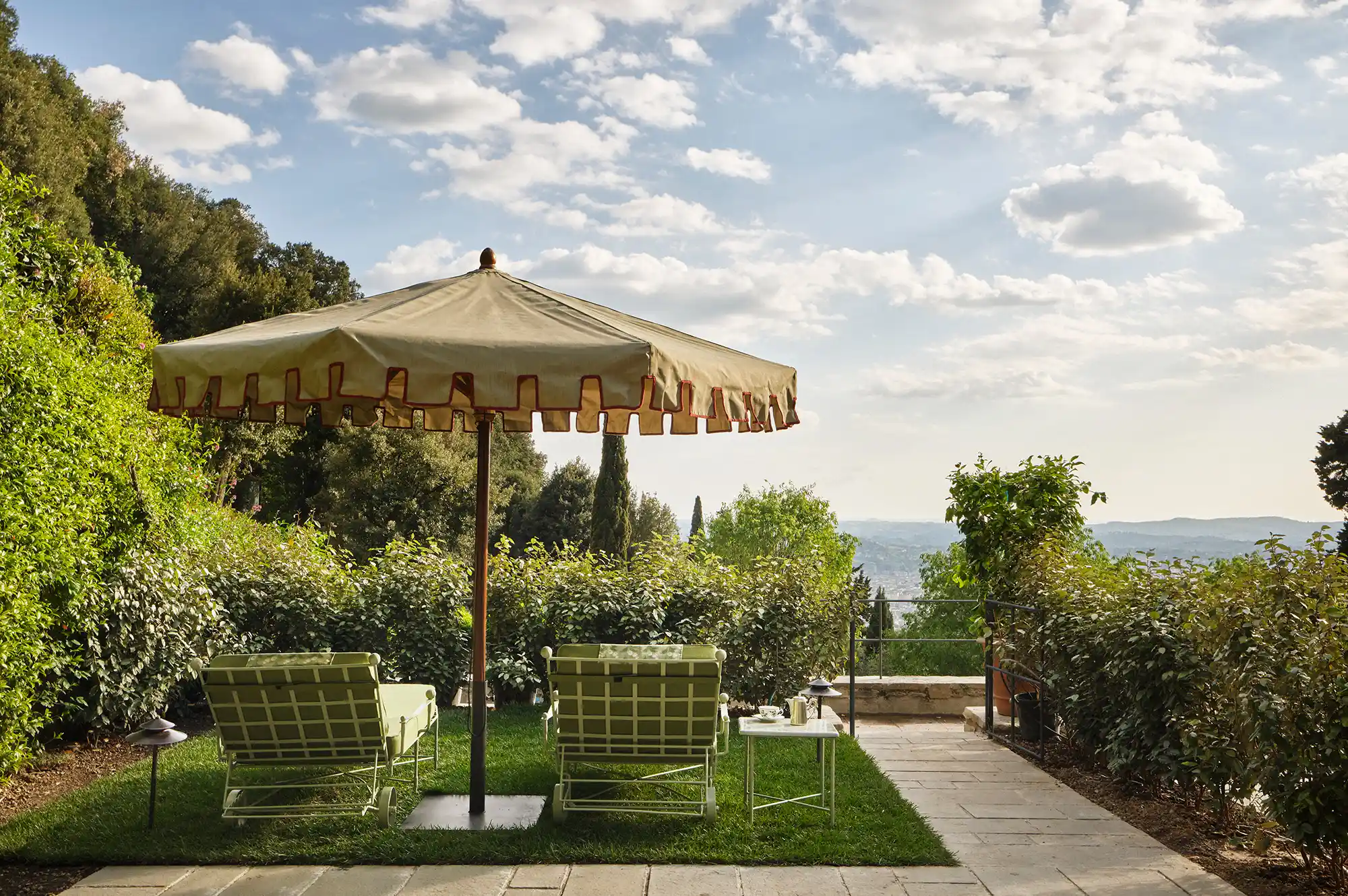 Two lounge chairs under a white umbrella overlooking a panoramic view of the Florentine valley.