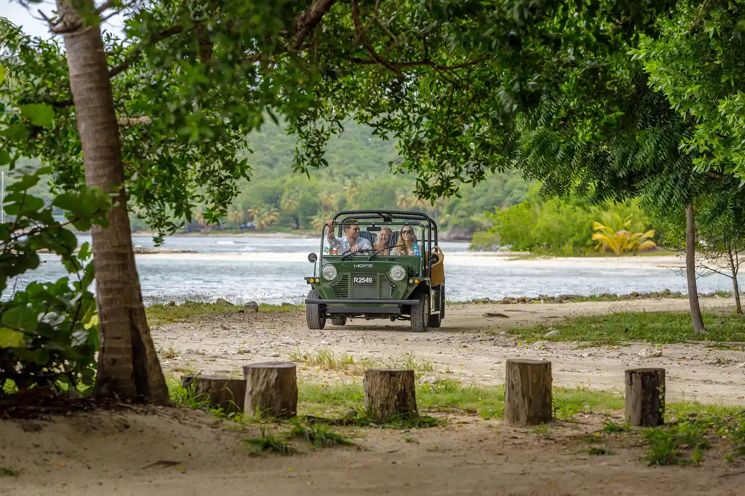 A small open-air utility vehicle parked on a dirt path near the tropical coastline.