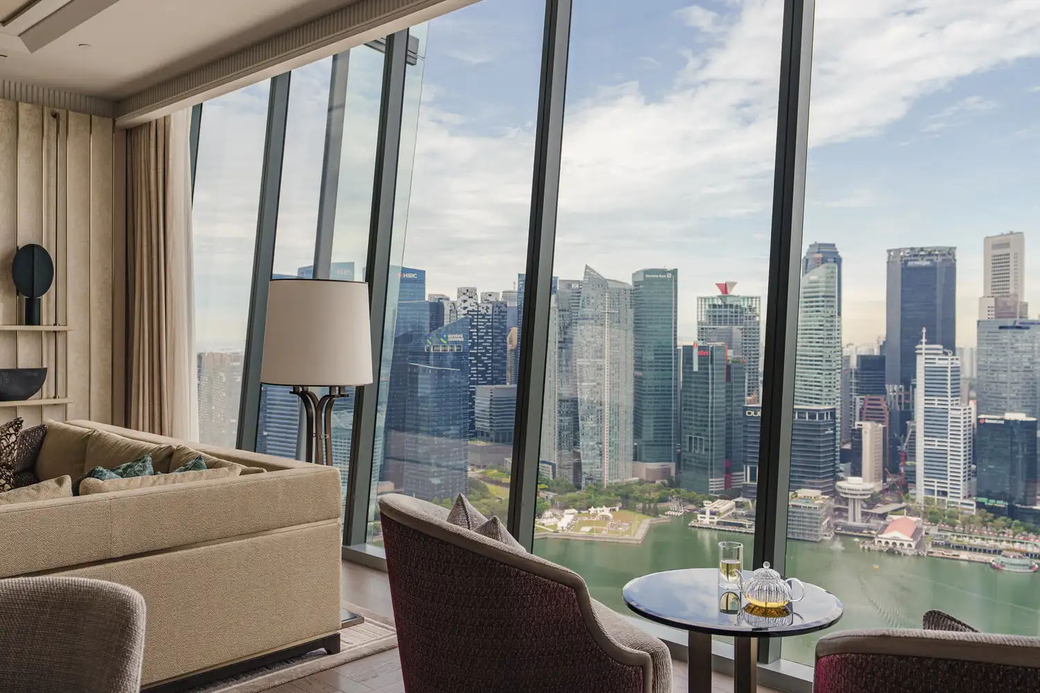 Interior of a luxury hotel suite with floor-to-ceiling windows overlooking the Singapore city center.