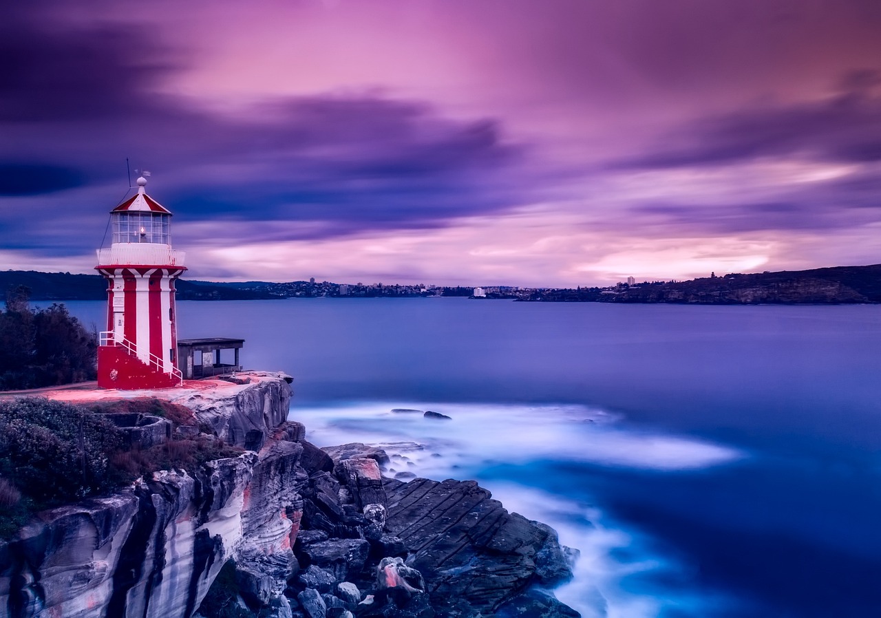 A red-topped lighthouse standing on a dramatic cliff edge at sunset.