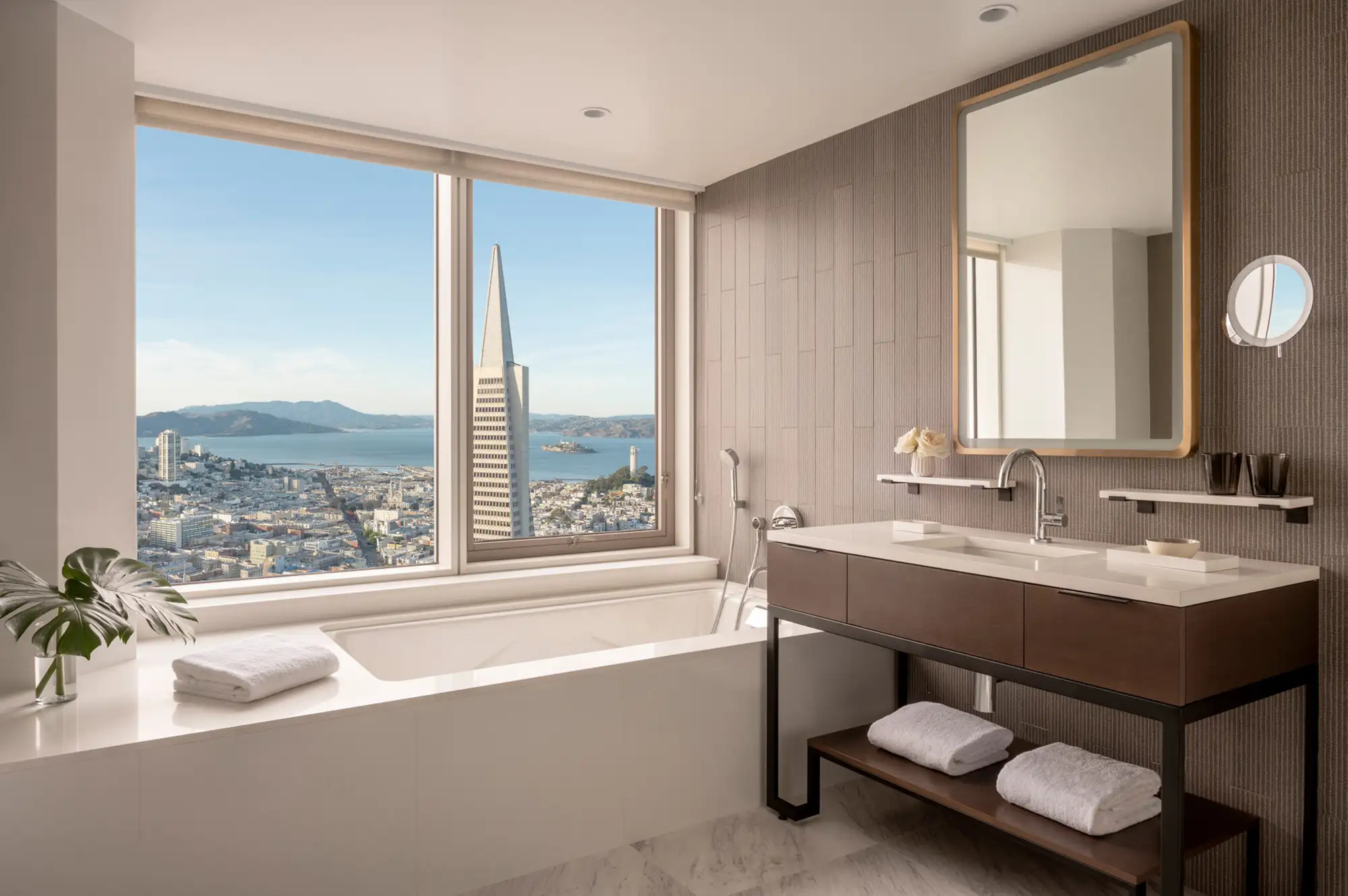 A luxury hotel bathroom featuring a large soaking tub with a direct view of the San Francisco skyline and Transamerica Pyramid.