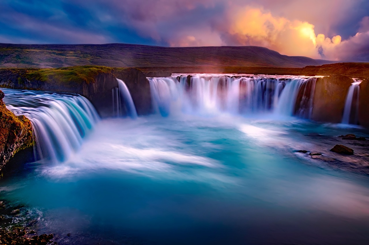 A lone figure standing in front of a massive Icelandic waterfall with a rainbow