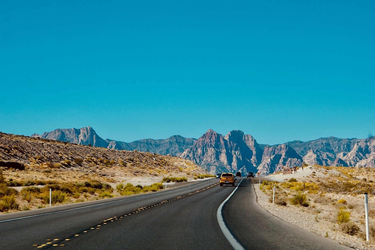 An empty scenic highway stretching toward distant mountains under a blue sky.