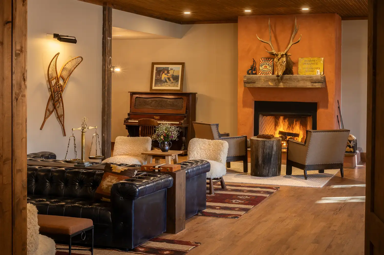 A spacious lodge lounge with a piano, leather armchairs, and rustic decor including antlers and a fireplace.