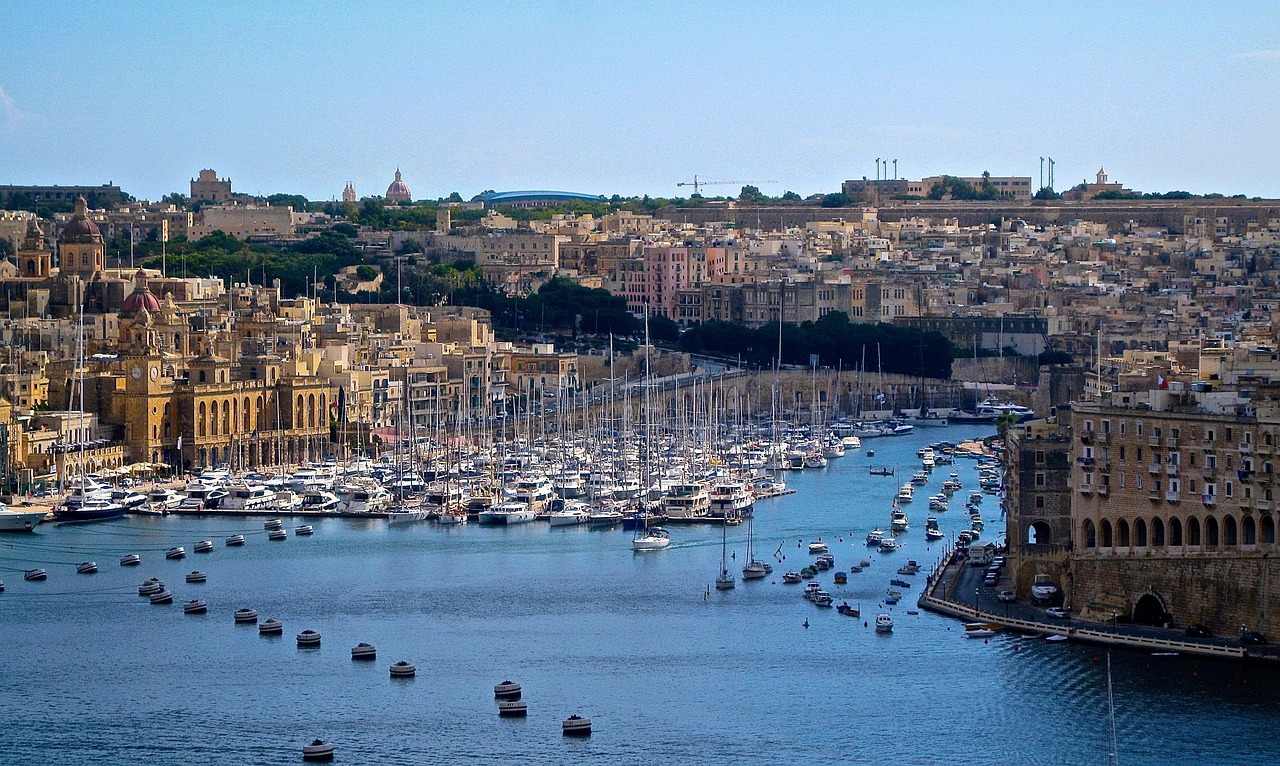 A colorful Mediterranean coastal town with small boats in the harbor and ancient architecture.