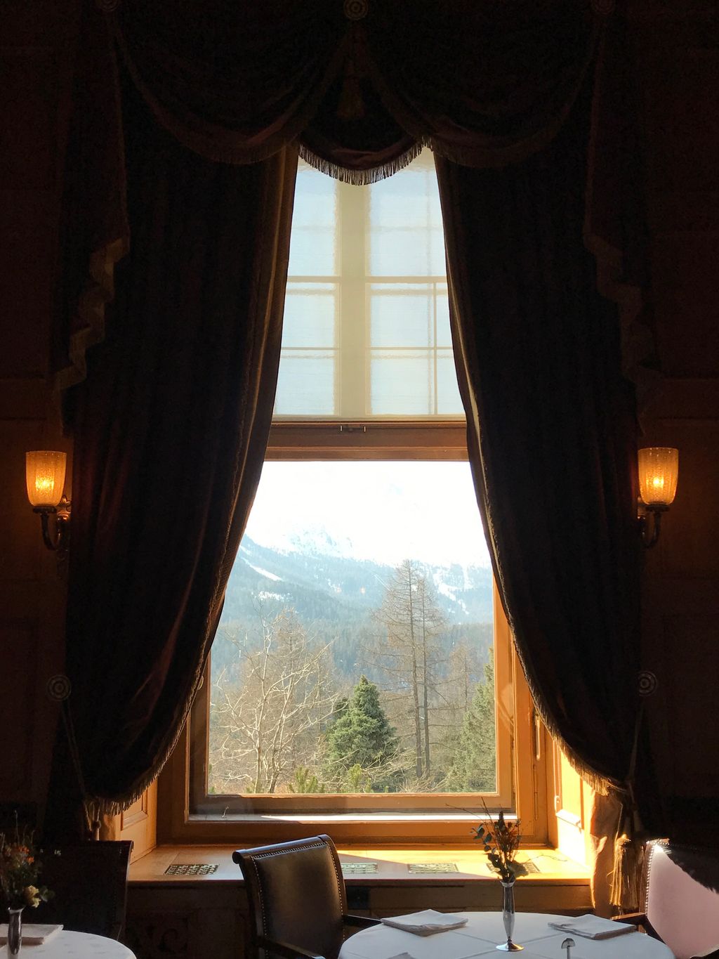 Luxury hotel interior in St. Moritz with a view of the Swiss Alps through a window.