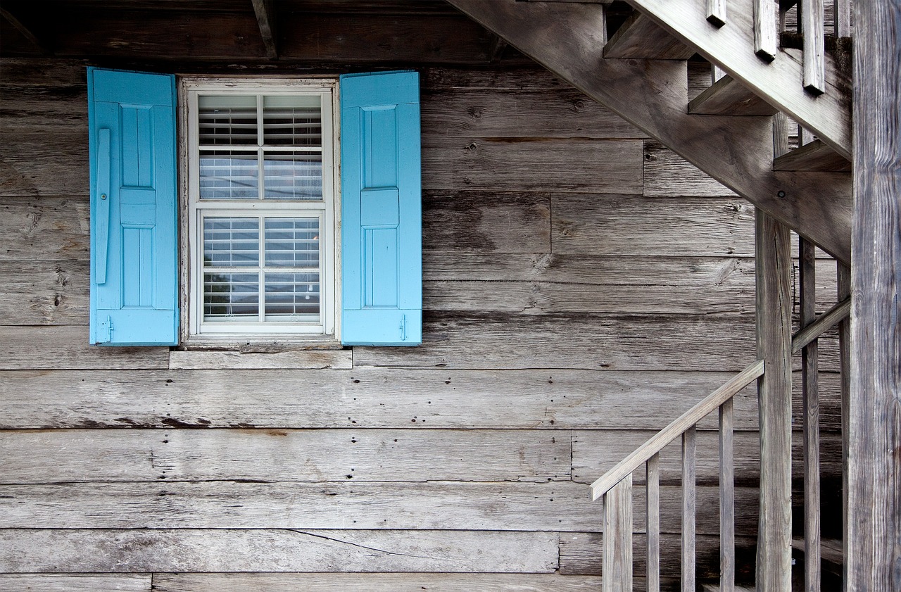 Historic wooden lodge with a porch overlooking a calm blue lake.