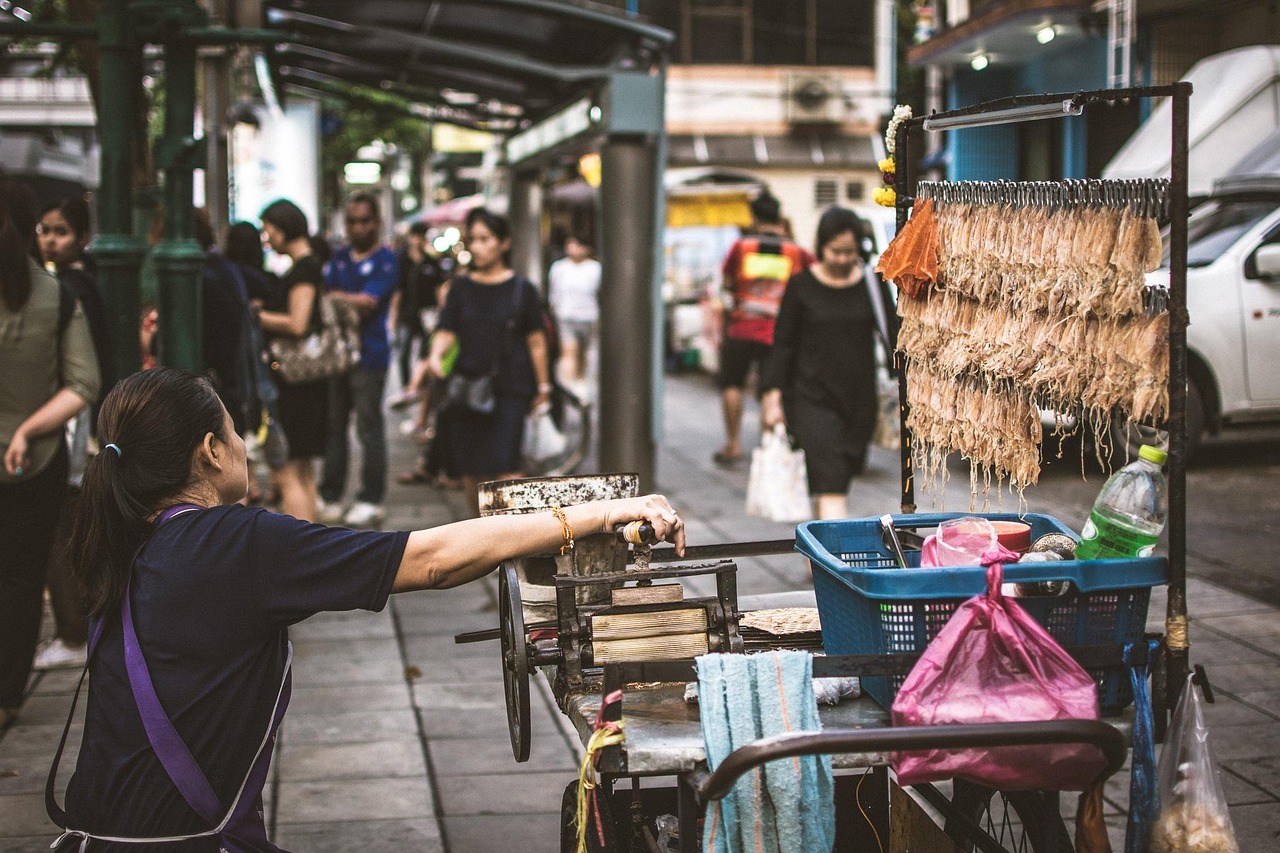 A bustling outdoor food court with various stalls and people dining.