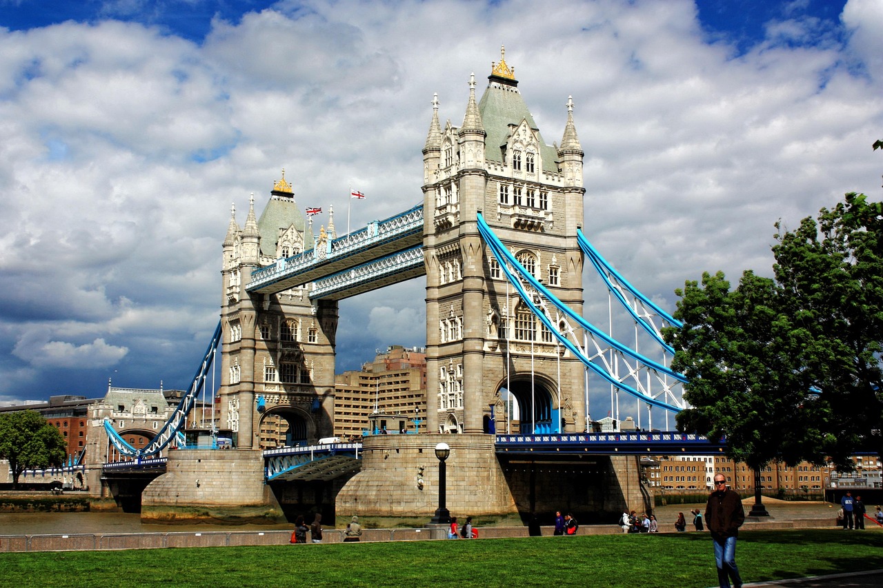A wide angle shot of Tower Bridge against a bright blue sky with a red double-decker bus