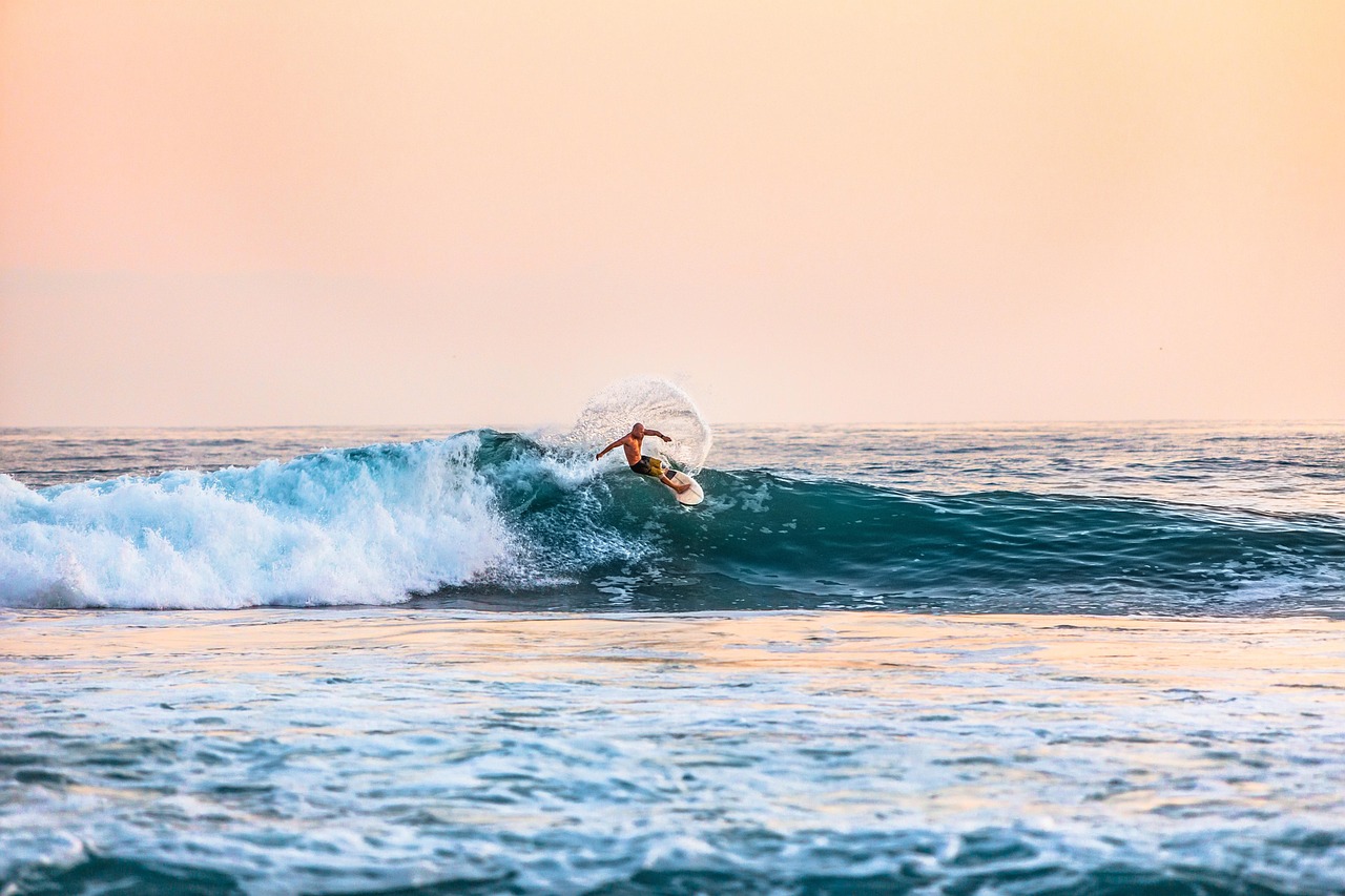 A surfer riding a gentle longboard wave at a golden beach