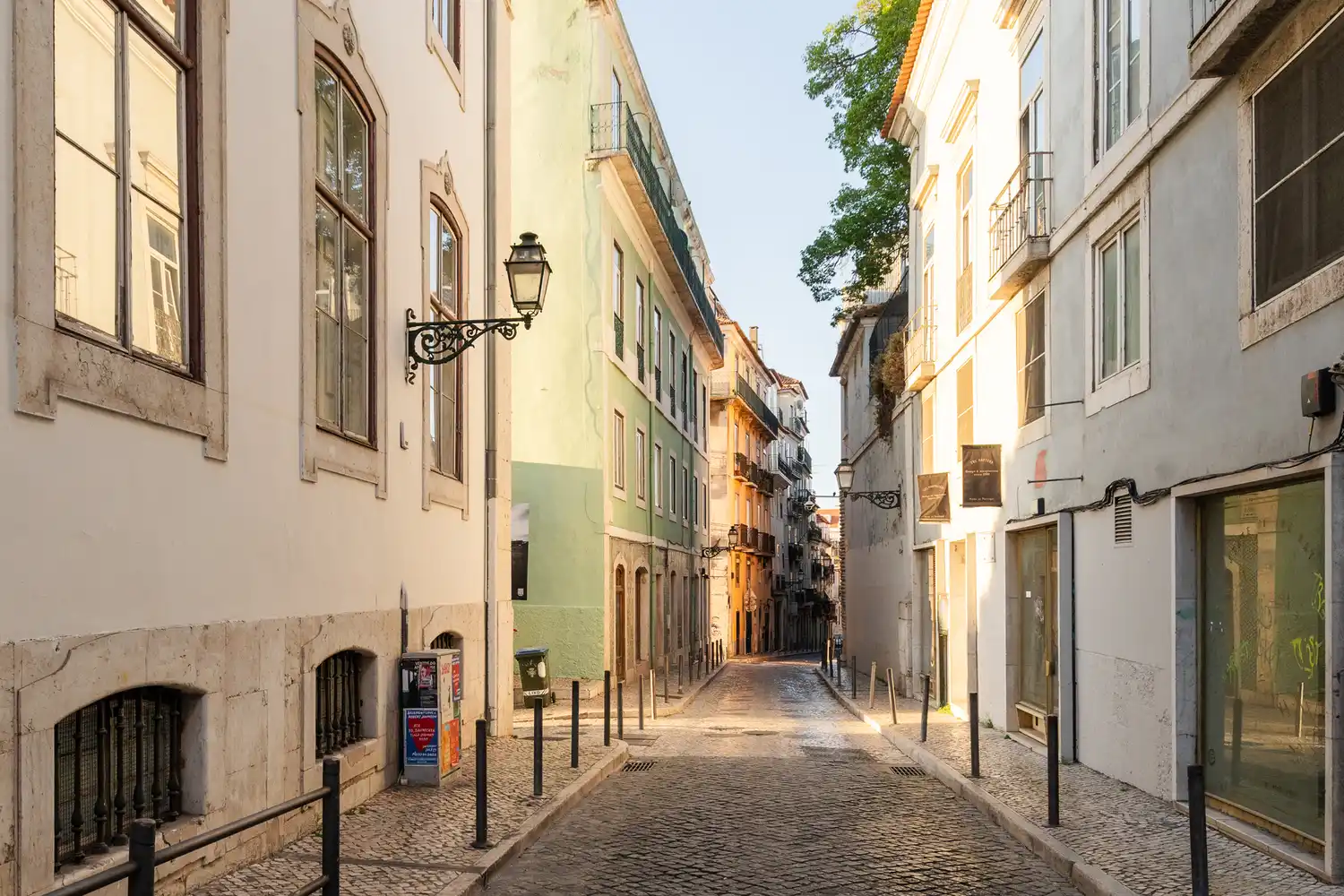 A narrow, bright cobblestone street in Lisbon with tall traditional buildings.