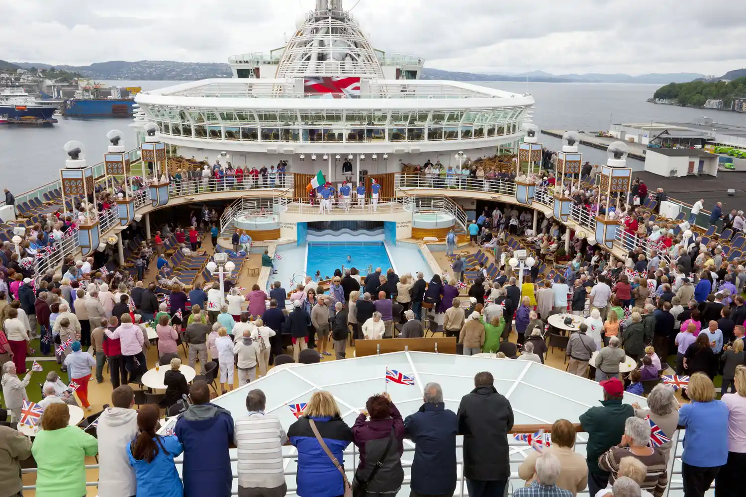 A crowded pool deck on a cruise ship filled with passengers near the water.