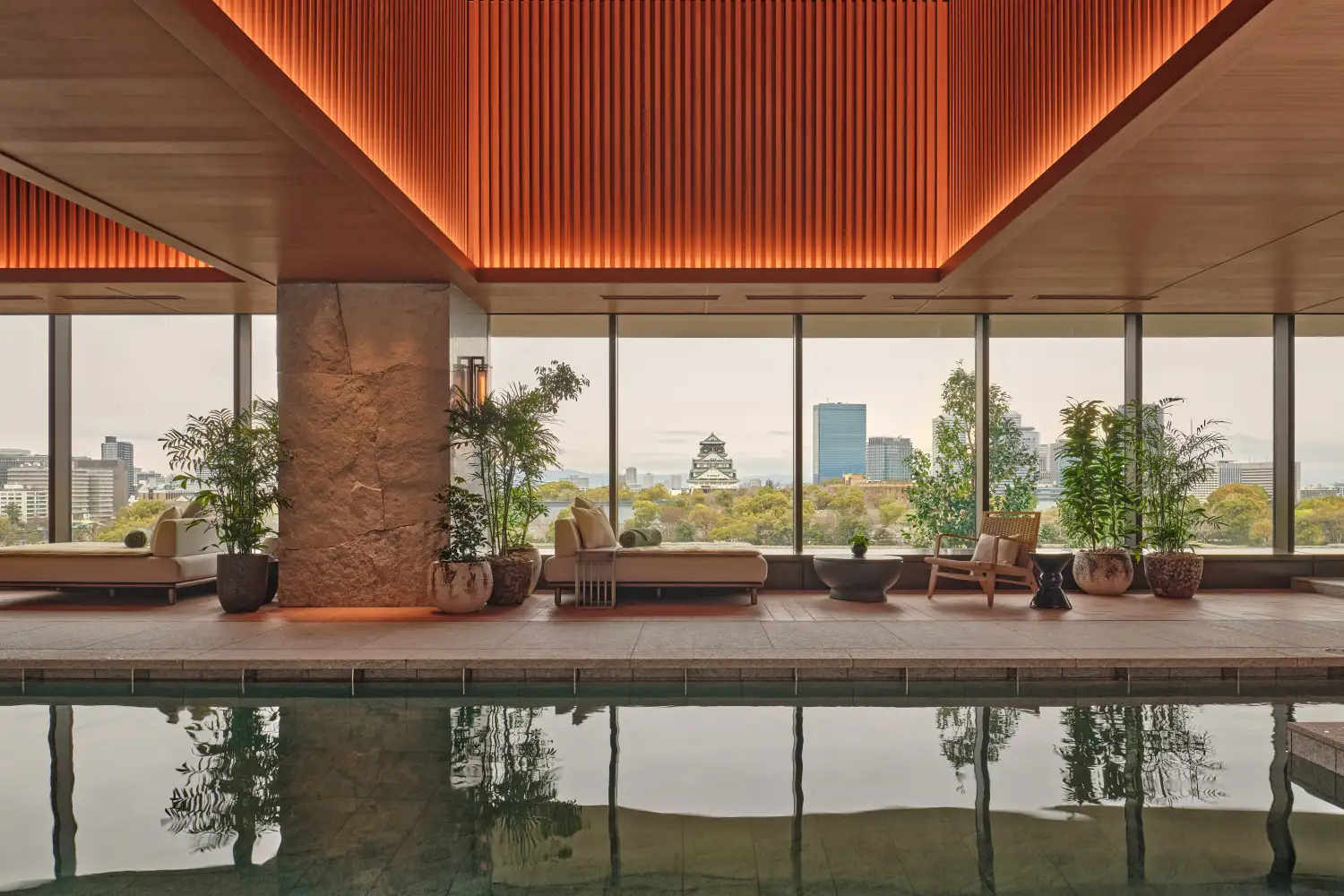 A sleek indoor wellness pool at Patina Osaka with large windows overlooking the city skyline and a historic castle.