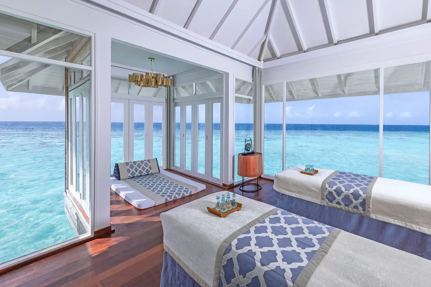 Interior of a spa treatment room with massage beds facing large windows with ocean views.