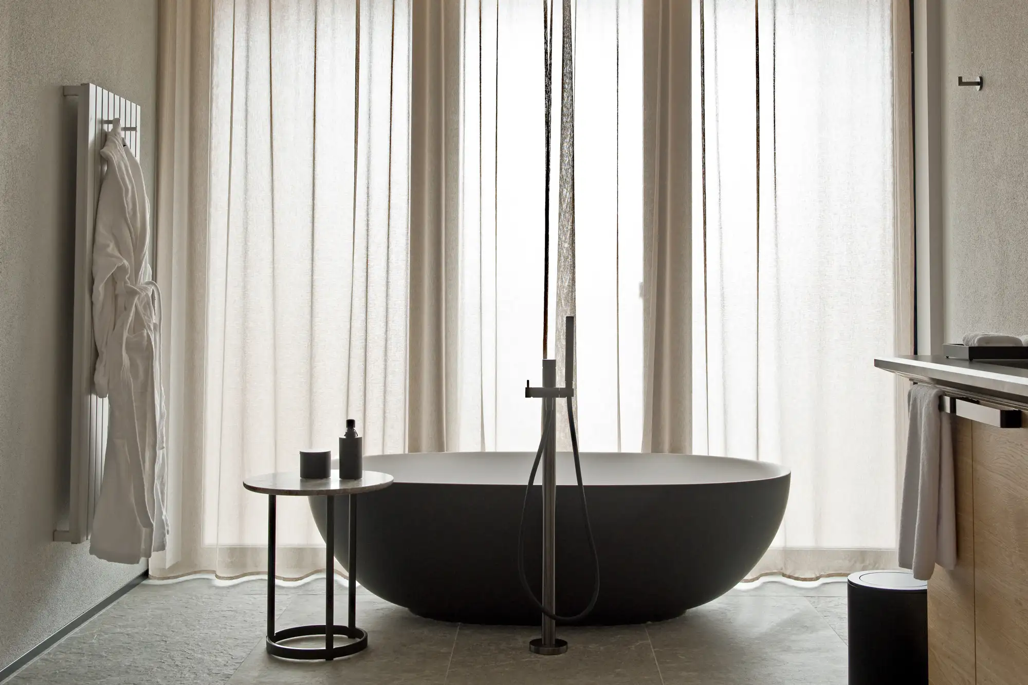 A minimalist luxury bathroom featuring a freestanding white bathtub and sheer curtains.