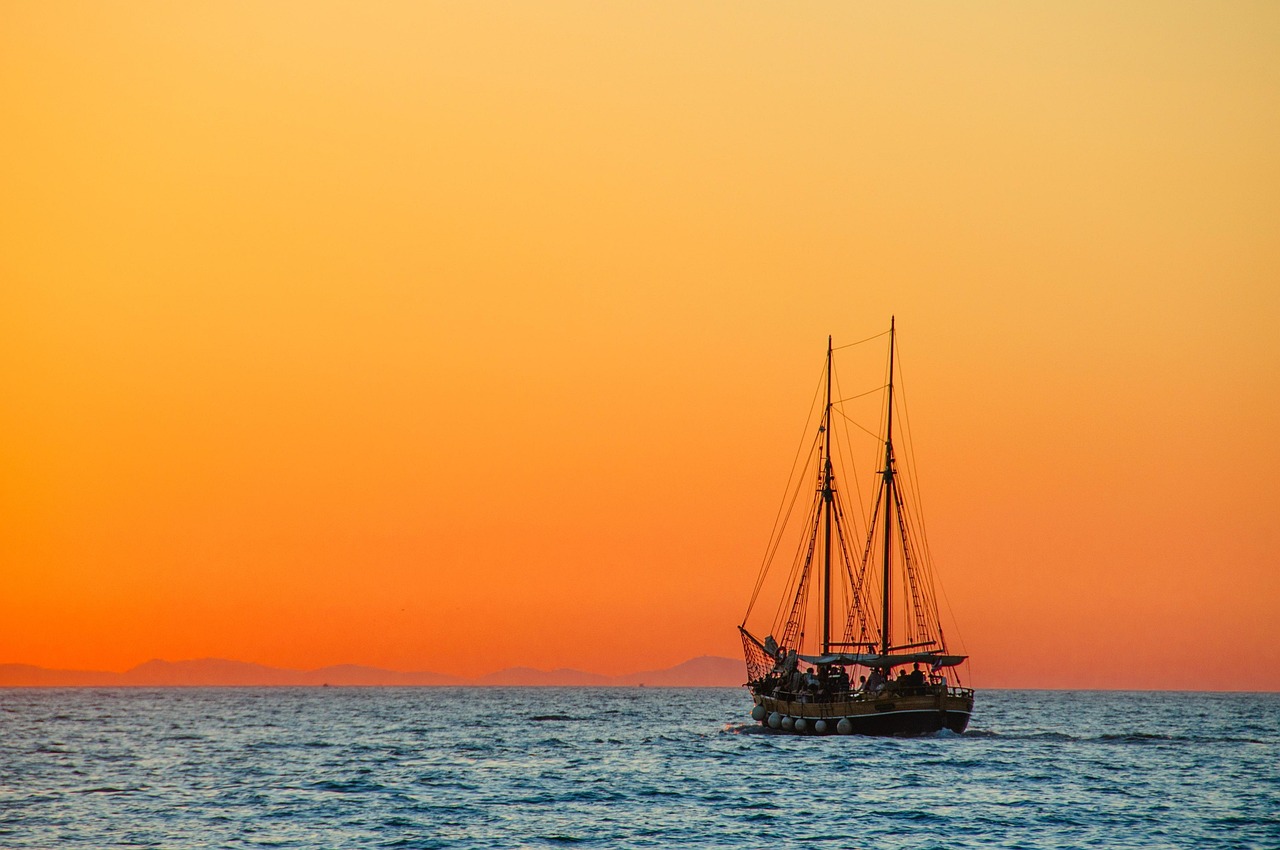 A wooden boat sailing on the sea during a golden sunset.