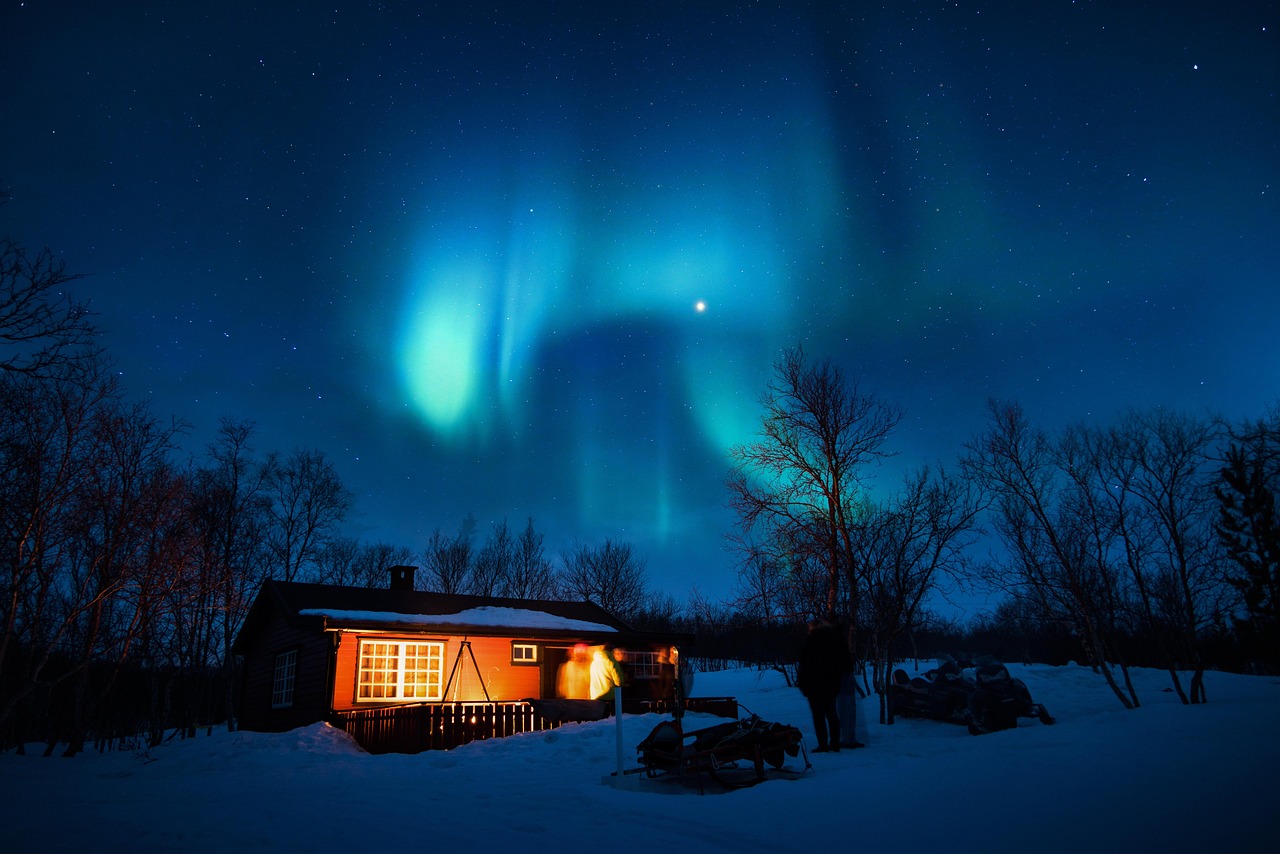 The Aurora Borealis glowing over a cozy wooden cabin in the snow.