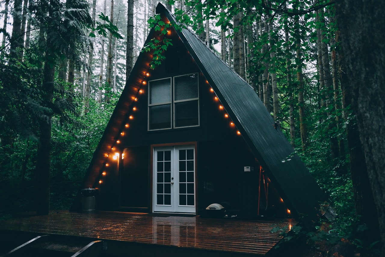 A modern wooden cabin with a large wrap-around deck surrounded by tall pine trees.