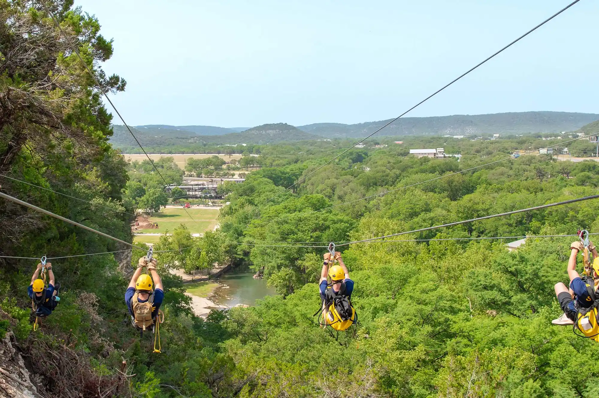 People participating in a zipline activity over a lush green forest canopy.