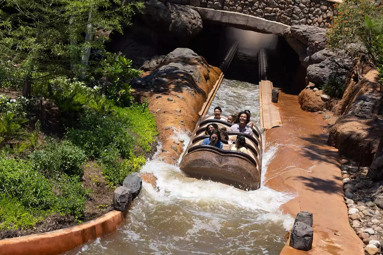 Guests riding a log flume through a lush, colorful swamp scene in Tiana's Bayou Adventure.