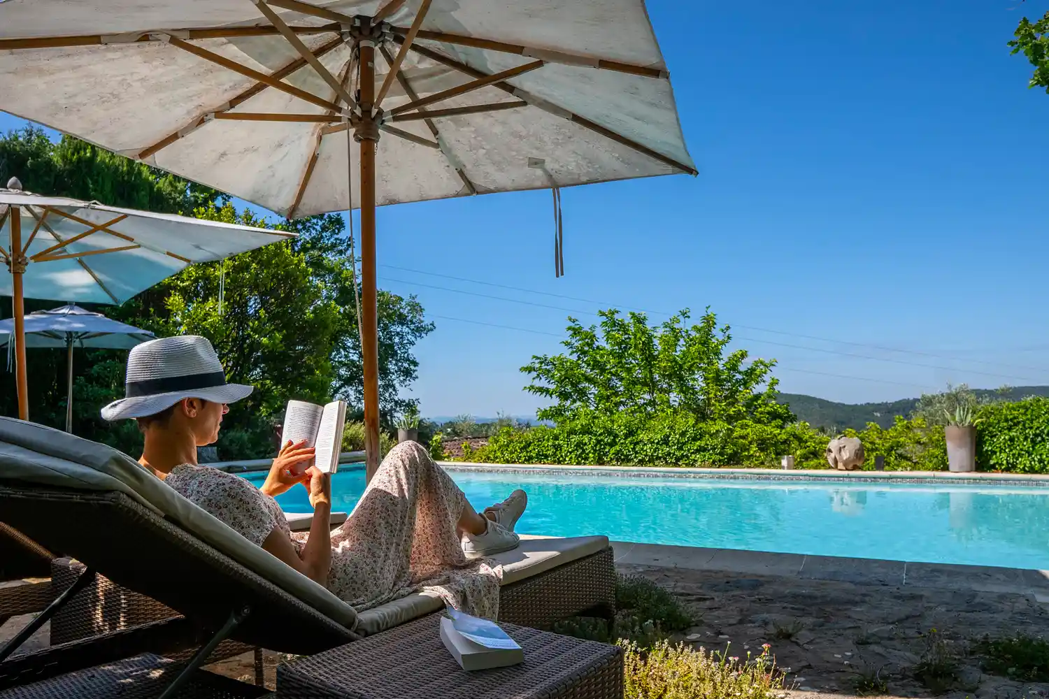 A woman relaxes on a lounge chair with a book by a pristine swimming pool at a French Riviera hotel.