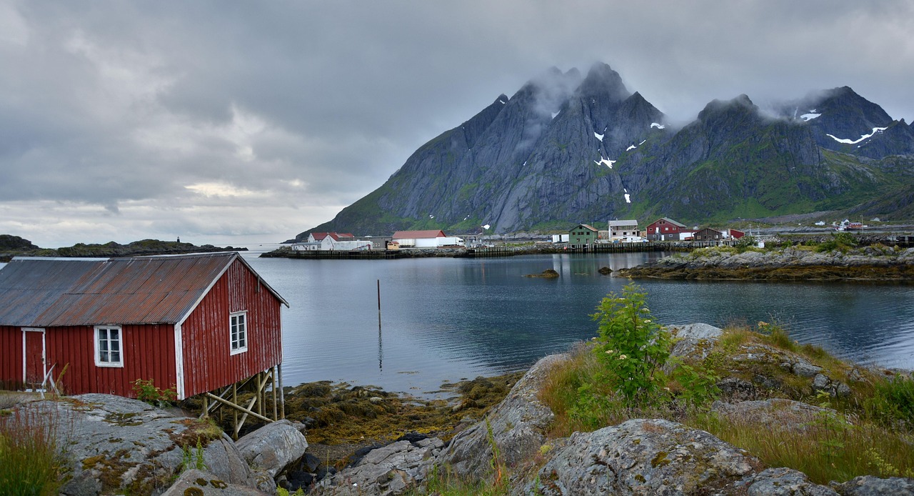 Traditional red fishing huts (rorbuer) against dramatic snowy mountains in Norway