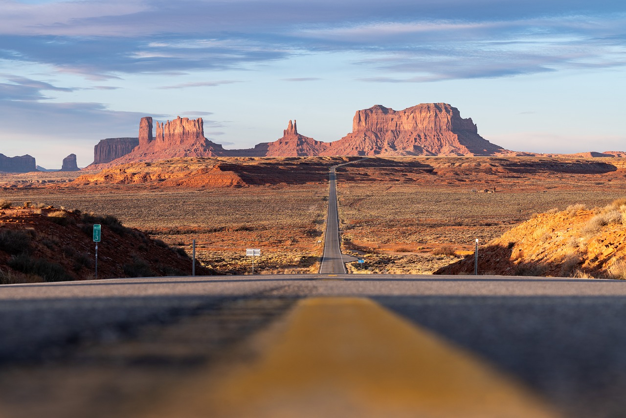 Long straight highway leading towards red rock formations under a blue sky.