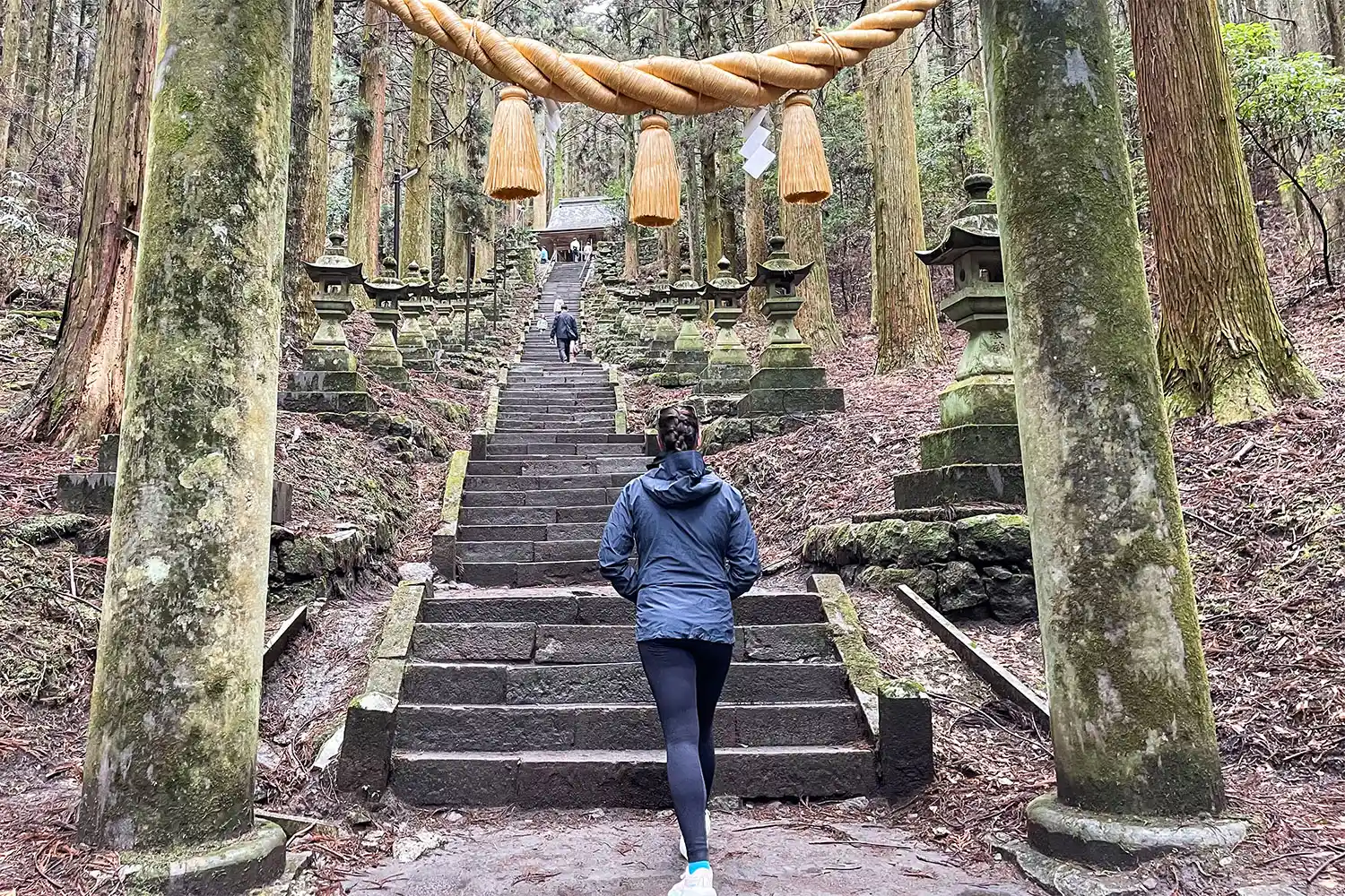 A person walking up a set of steep stone stairs while wearing a travel backpack.