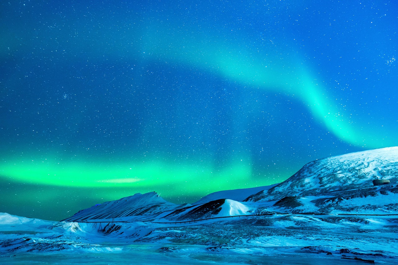 Bright green aurora borealis dancing over a snowy mountain range at night.