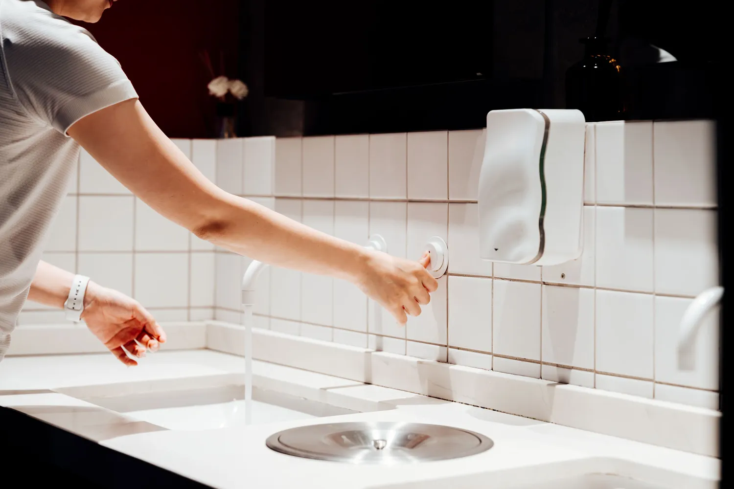 Hands being washed with soap under a running faucet at a public sink.