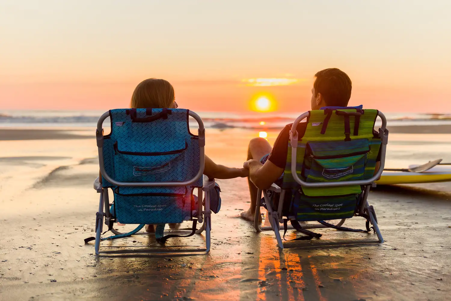 A couple sitting in beach chairs watching the sunset over the Atlantic ocean.