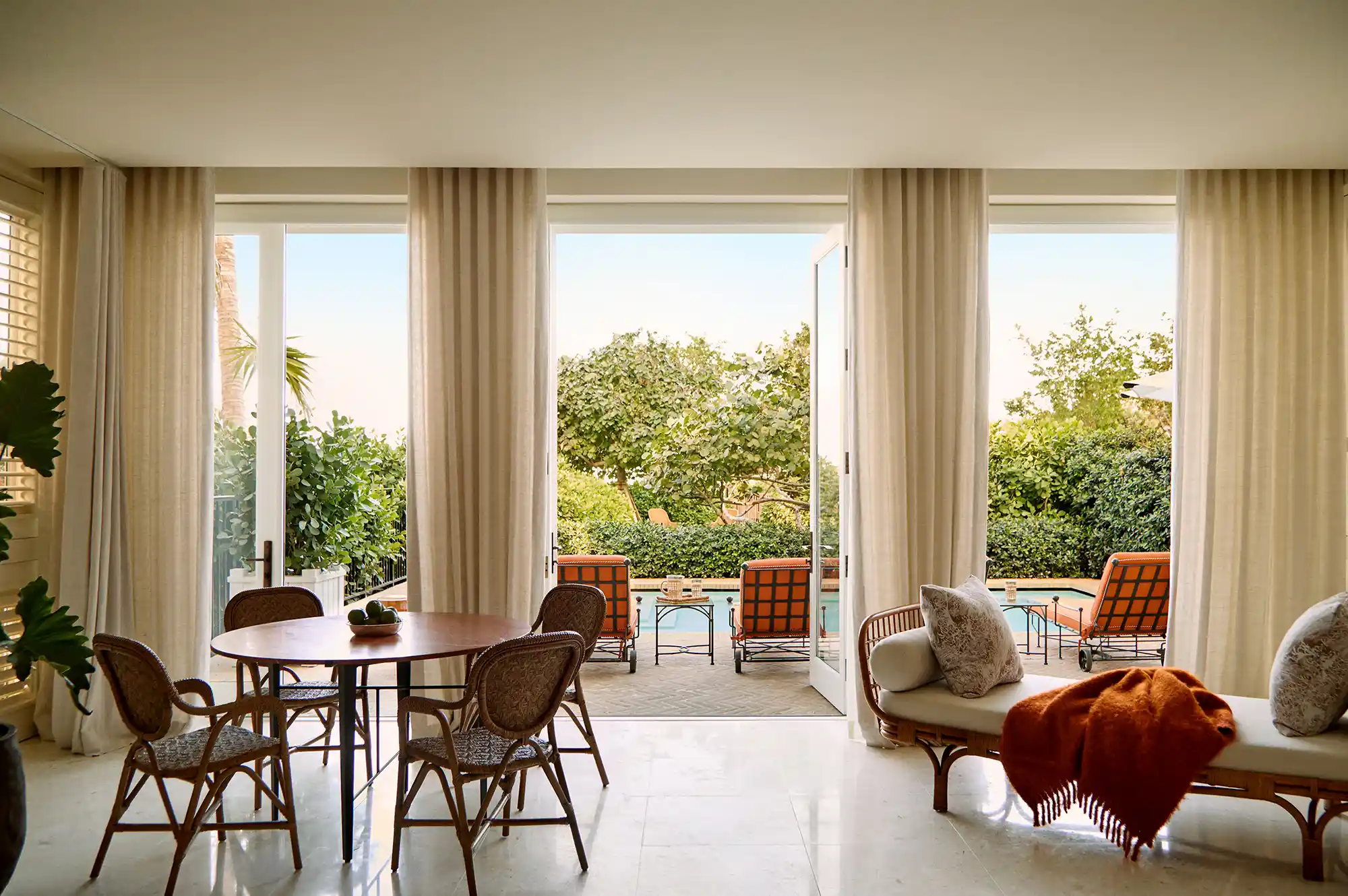 An open-plan living area leading to a sun-drenched patio with a private pool and tropical landscaping.