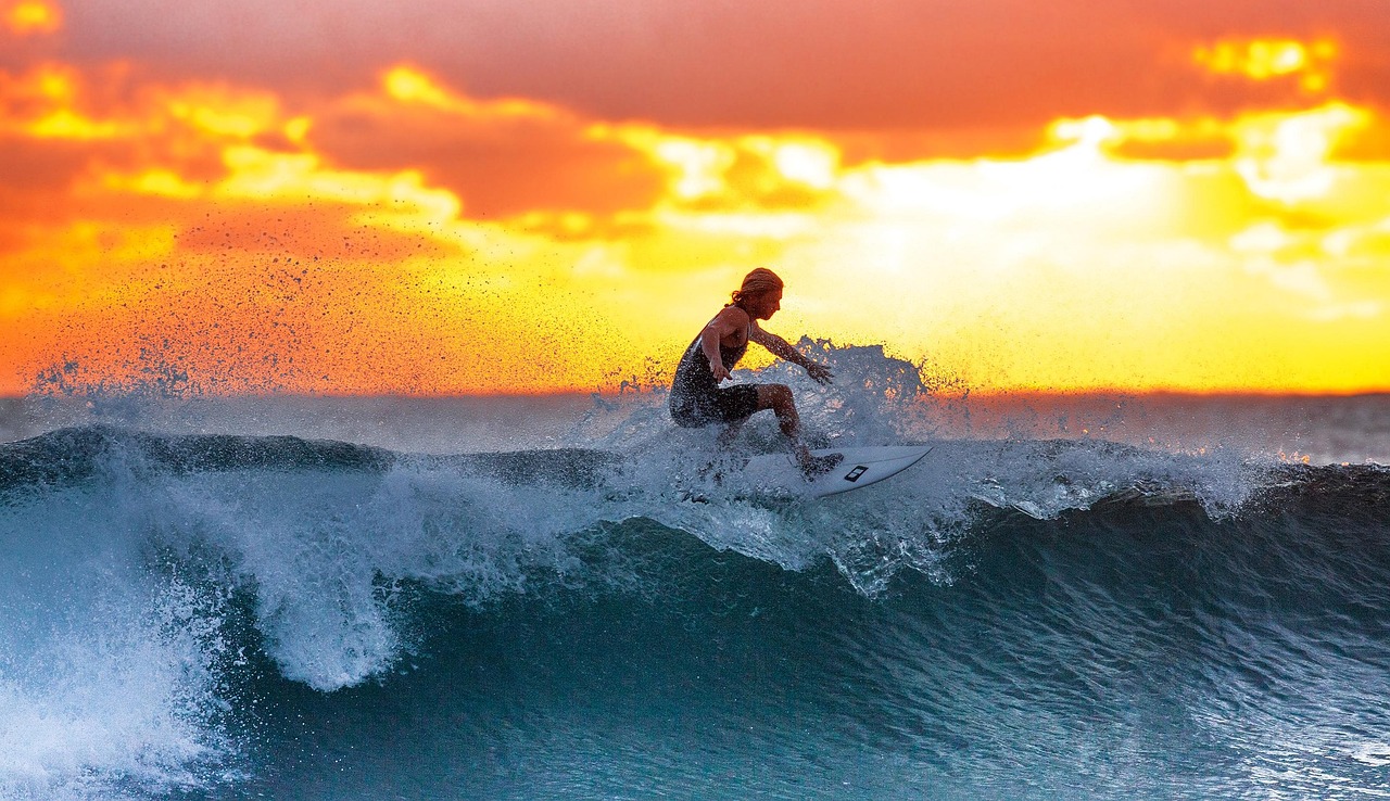 A female surfer sitting on a board wearing a stylish long-sleeve floral rash guard.
