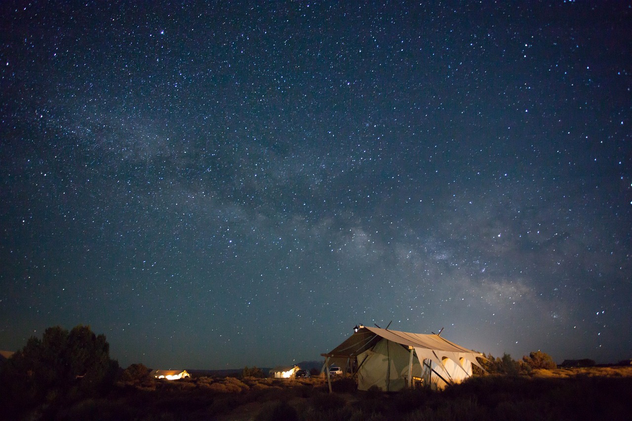 The Milky Way galaxy visible over a darkened landscape with a tent silhouette.