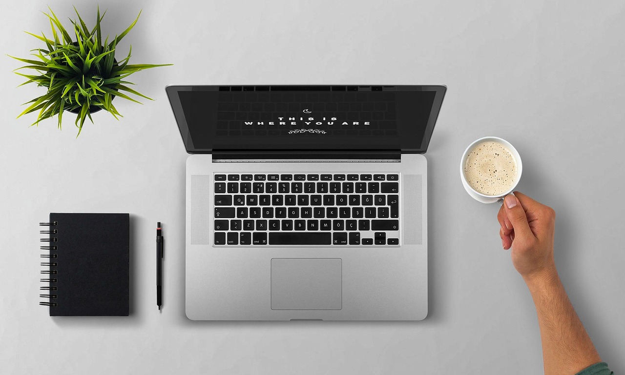 A person using a laptop at a table with a cup of coffee nearby