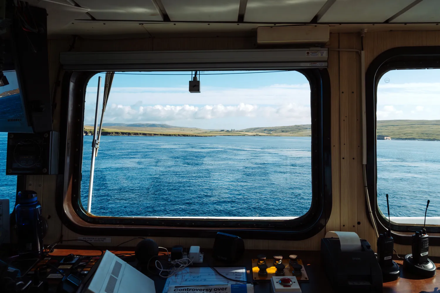 View from a ferry control room looking out over a waterway toward a distant green island.